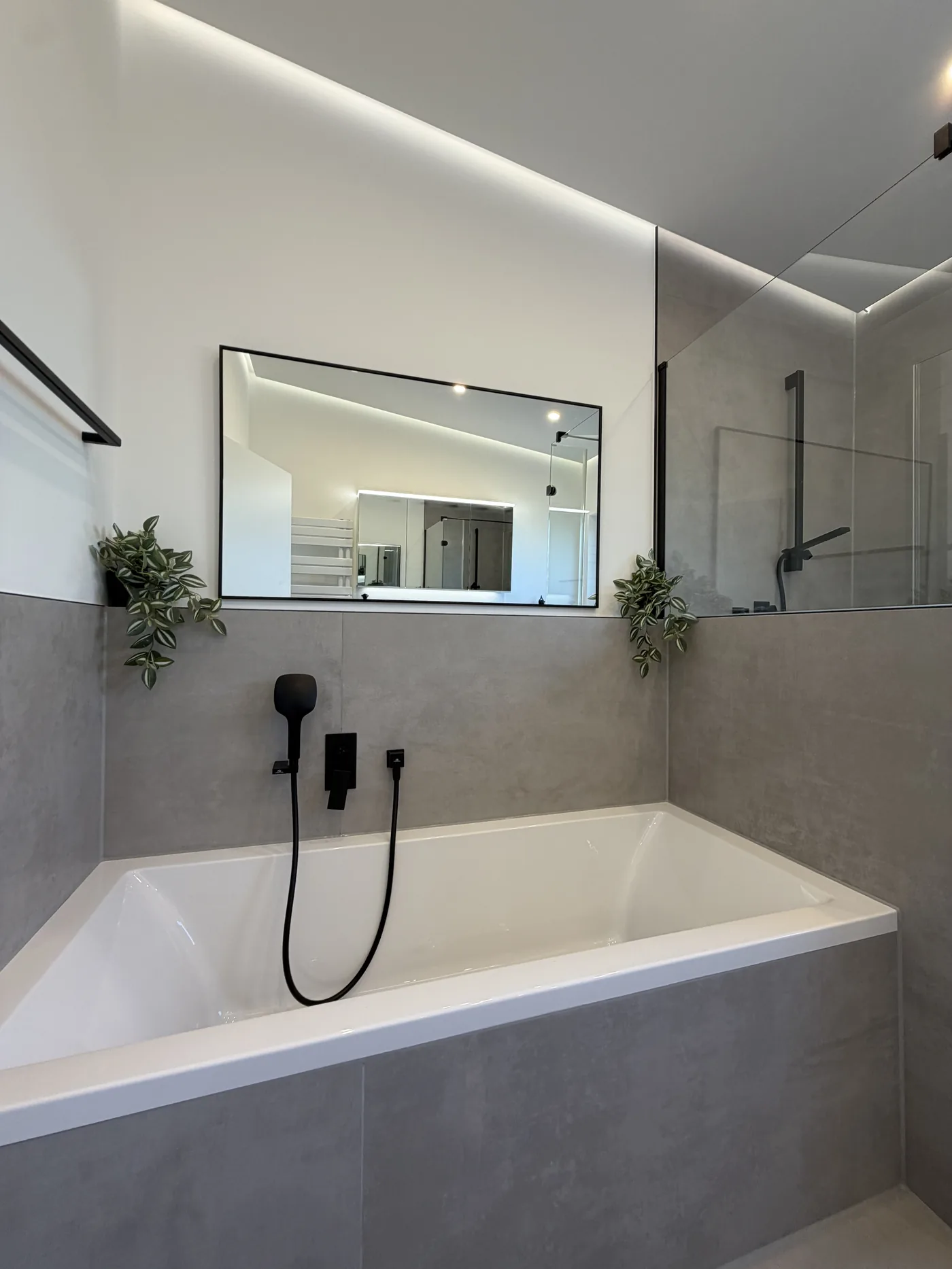 Fertiggestelltes Bad mit Badewanne, Betonlook-Fliesen und schwarzen Armaturen