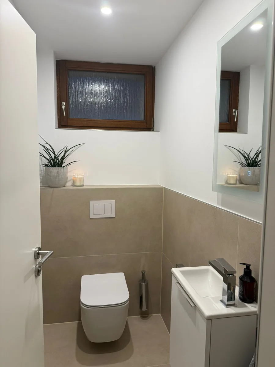 Renoviertes Gäste-WC mit großformatigen Fliesen und Wand-WC nach der Sanierung